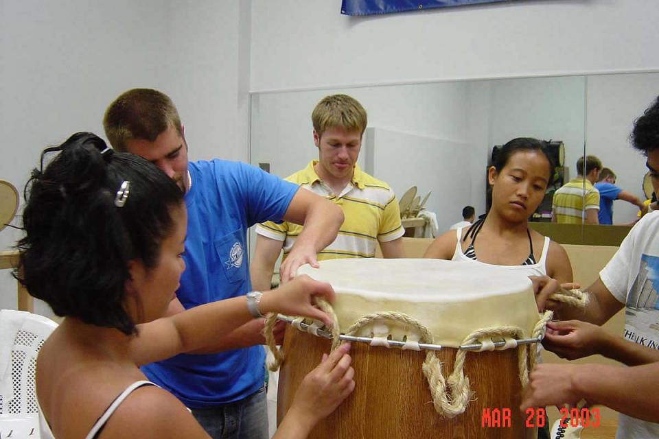 Members of Stanford Taiko lacing rope around dowels to prep drum head